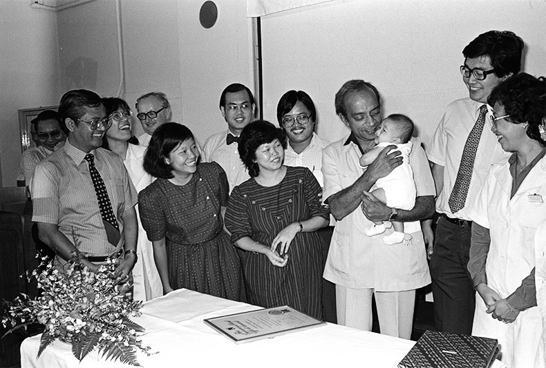 Professor S.S. Ratnam and his team receiving the Guinness Stout Effort Award for their work on in-vitro fertilisation, 1983. Ratnam is pictured here carrying Asia’s first “test-tube baby”, Samuel Lee Jian Wei, who was delivered by Ratnam and his team at the Kandang Kerbau Hospital on 19 May 1983. Samuel’s mother is standing beside Ratnam, while his father is behind her. Ministry of Information and the Arts Collection, courtesy of National Archives of Singapore.
